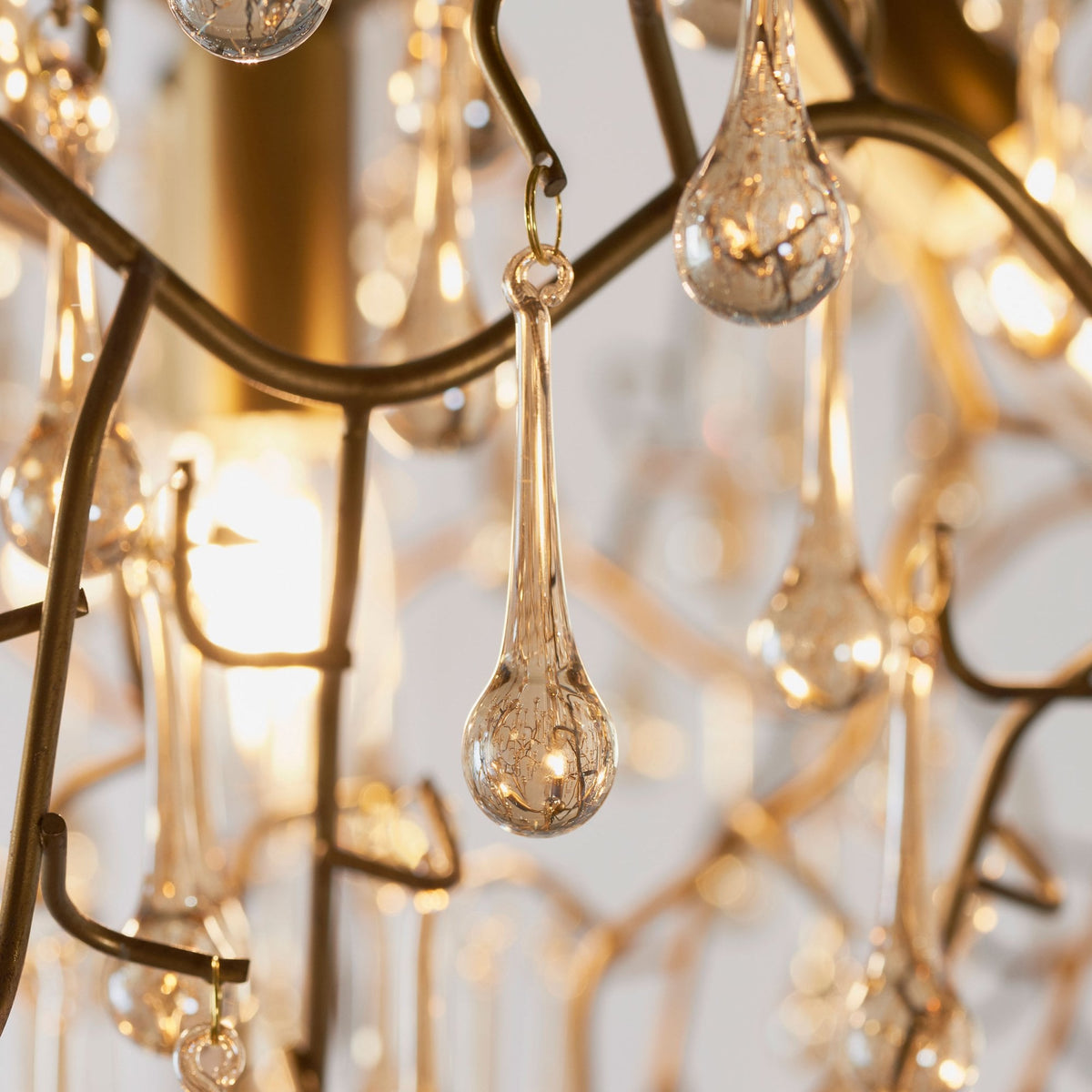 A detailed view of a single champagne-colored glass droplet hanging from the bronze chandelier's branch.