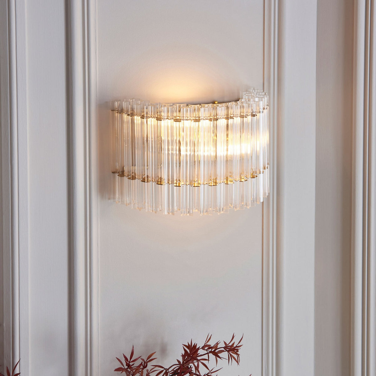 A close-up view of a curved glass and brass wall sconce with vertical fluted glass rods emitting a warm glow.
