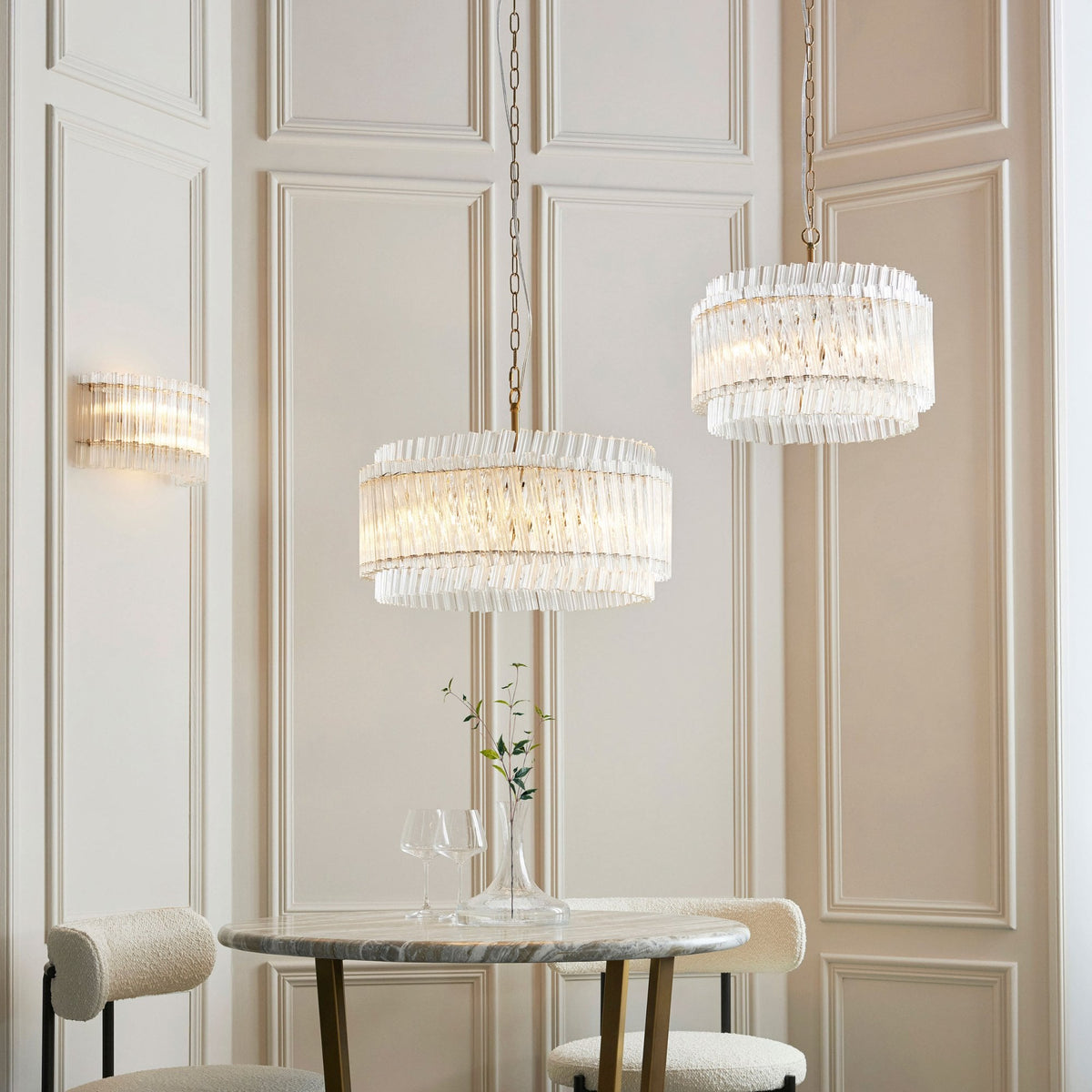 A sophisticated dining area featuring two matching glass pendant lights, a wall sconce, and a marble table.
