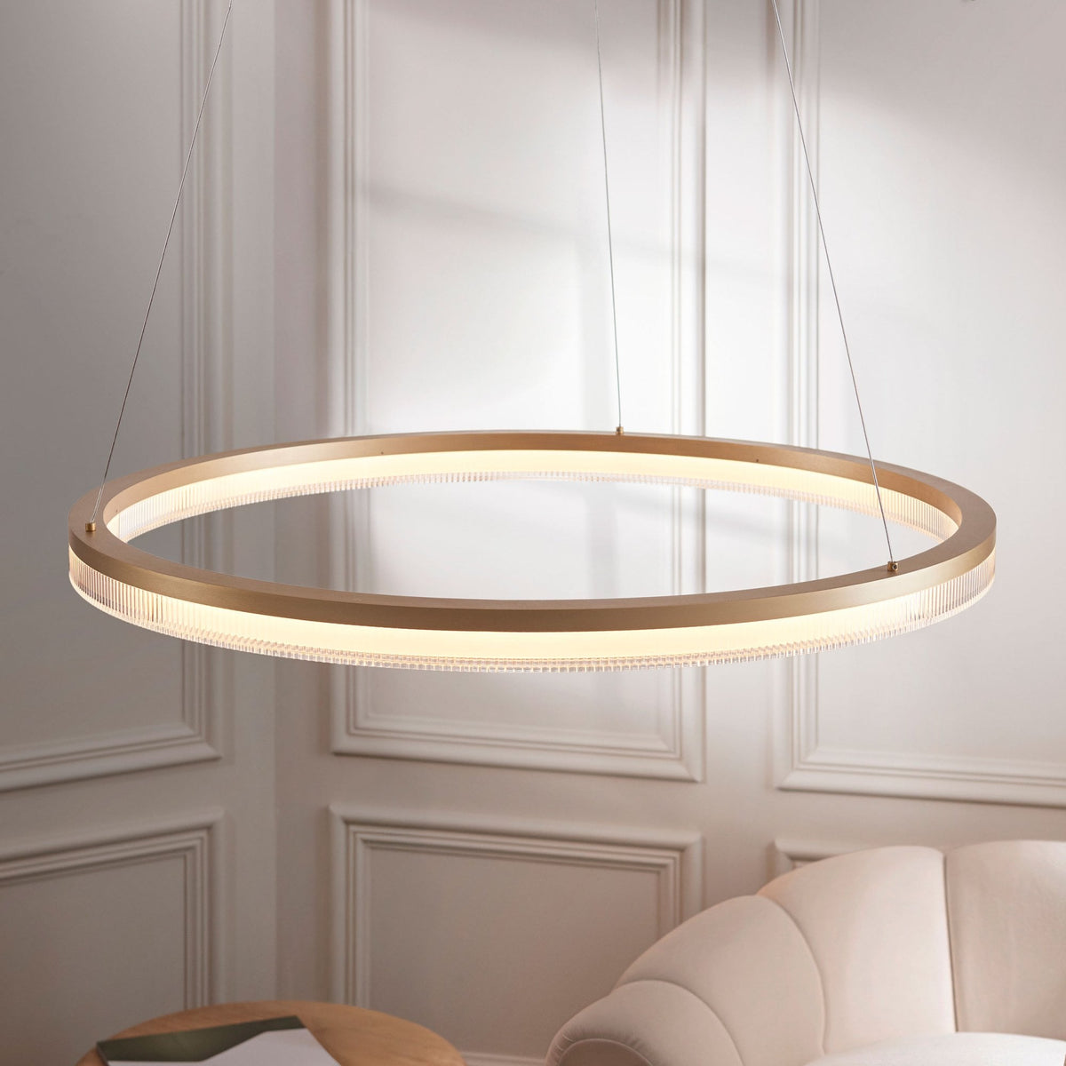 An illuminated gold ring-shaped chandelier hangs above a beige sofa, providing elegant lighting.