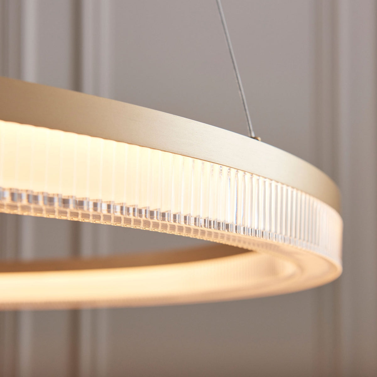 A close-up of the illuminated gold ring chandelier, showing the ribbed glass detail along its edge.