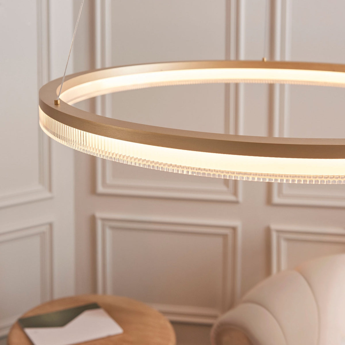 The illuminated gold ring chandelier with ribbed glass detail, casting a soft glow in a modern room.