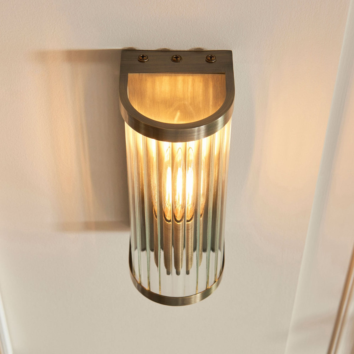 An overhead view of the gold-plated, wall-mounted light with a fluted glass shade, emitting a soft light.