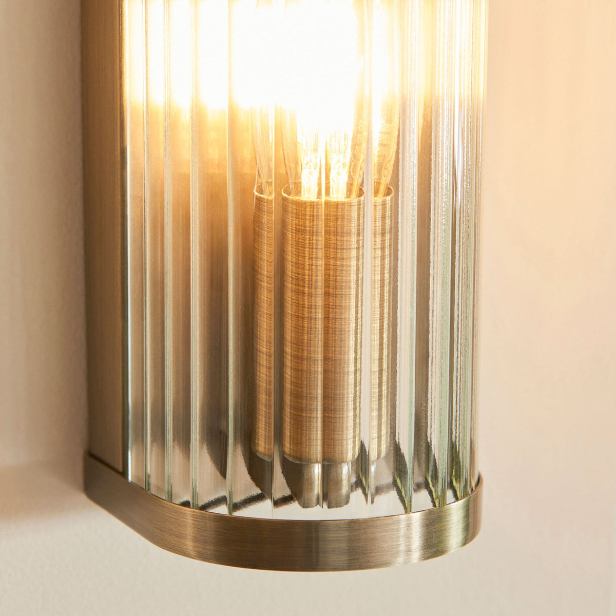 A detailed close-up of the fluted glass shade and gold-plated base of a wall-mounted light fixture.