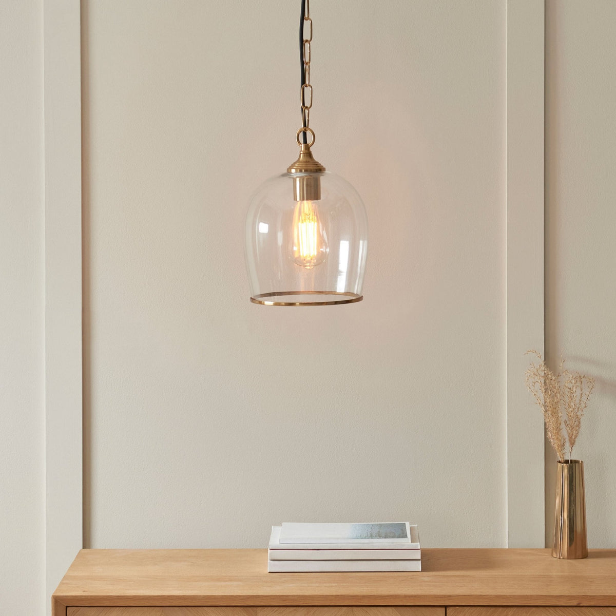 A close-up of a glass and brass pendant light hanging over a light wood console table with decorative items.