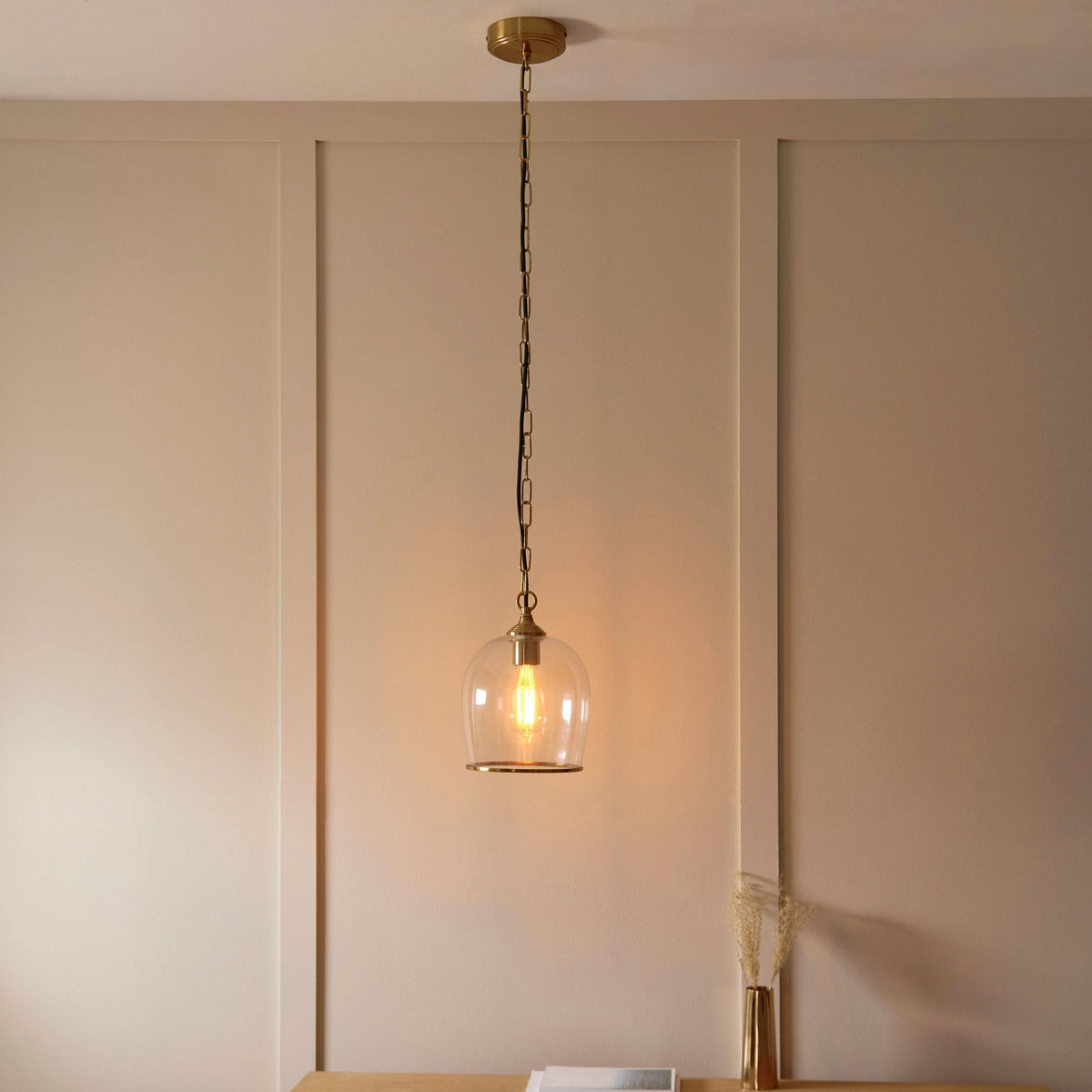 A full view of a glass and brass pendant light illuminating a neutral-toned room above a console table.