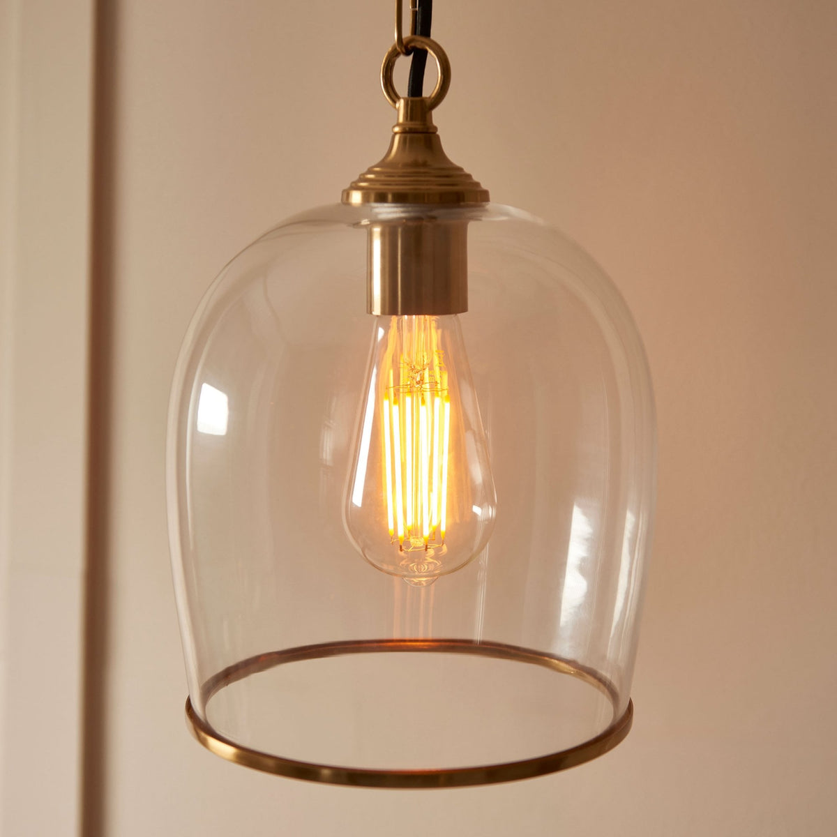 A detailed view of the clear glass shade, brass band, and visible filament bulb of the pendant light.