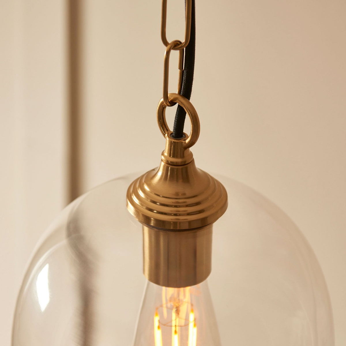 A close-up of the brass fixture connecting the chain to the clear glass shade and the exposed bulb.