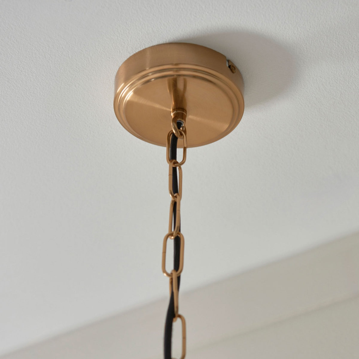A close-up of the round brass ceiling rose and the hanging chain of the pendant light fixture.