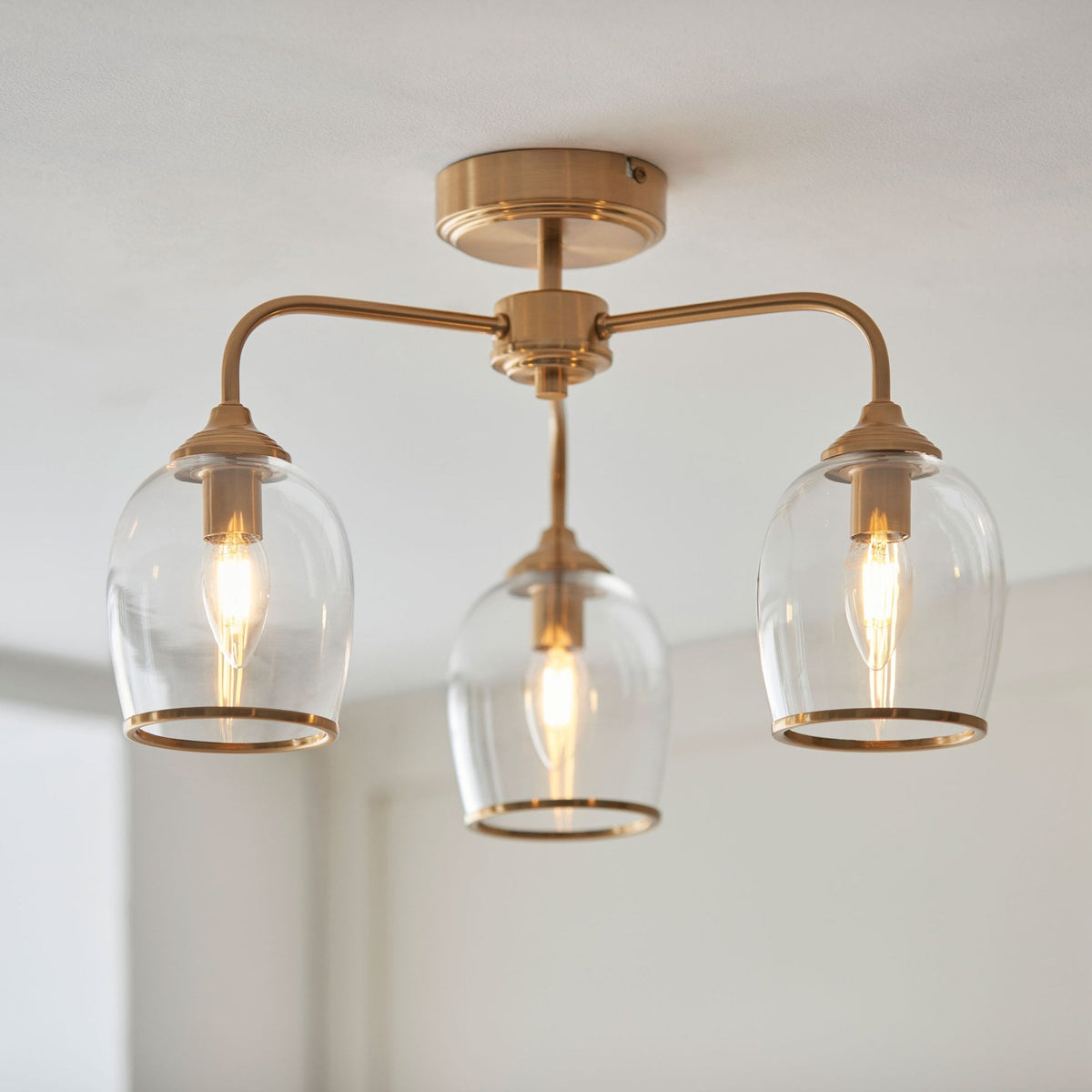 A close-up shot of a ceiling light fixture with three clear glass shades and a brass finish.