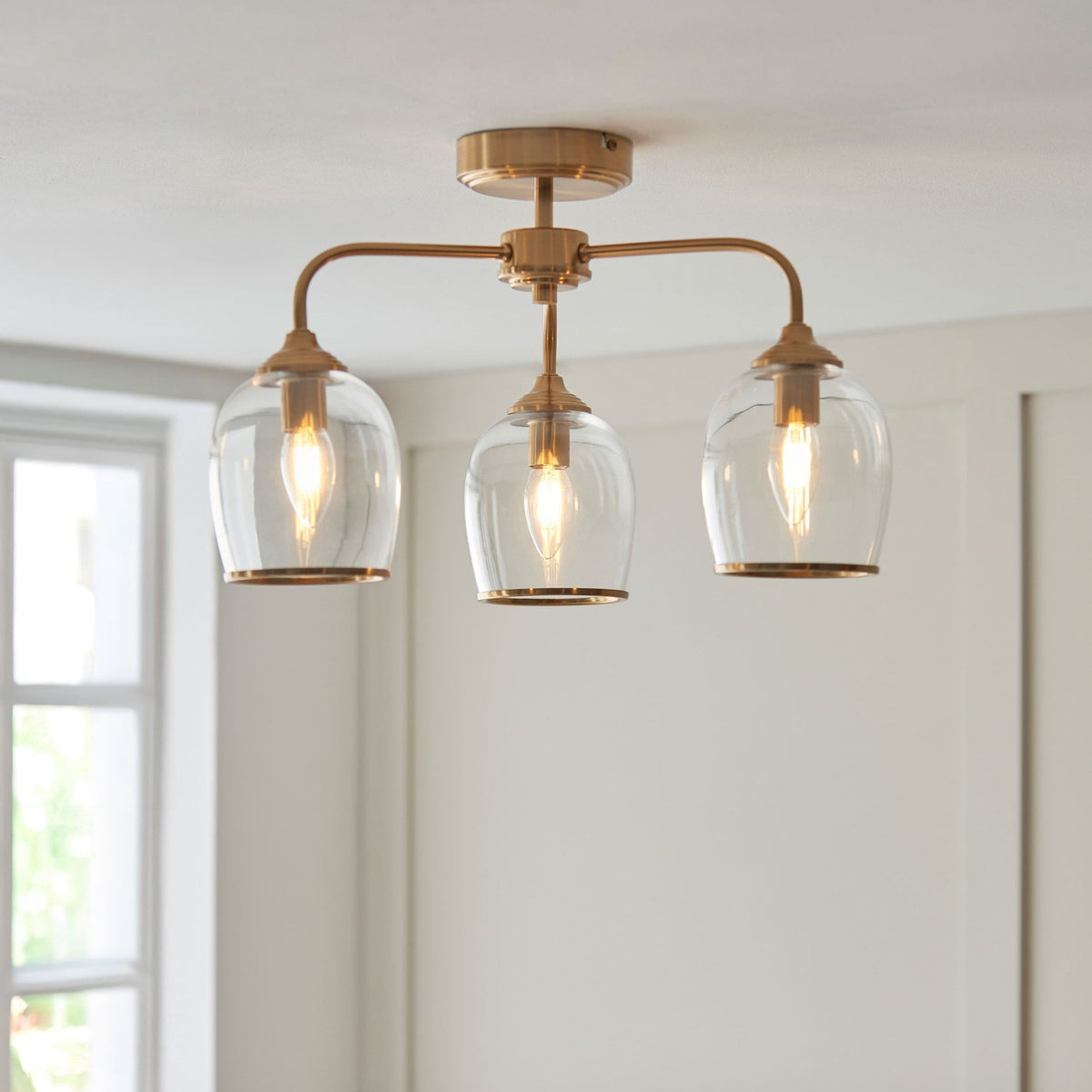 A three-light ceiling fixture with clear glass shades and a brass finish illuminates a bright room.