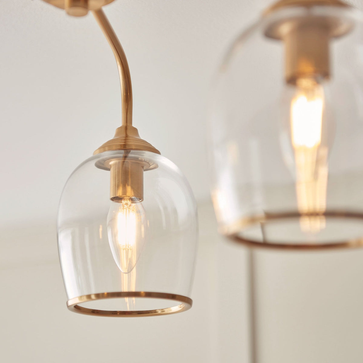 A close-up shows a single clear glass shade with a brass rim and a visible filament bulb.