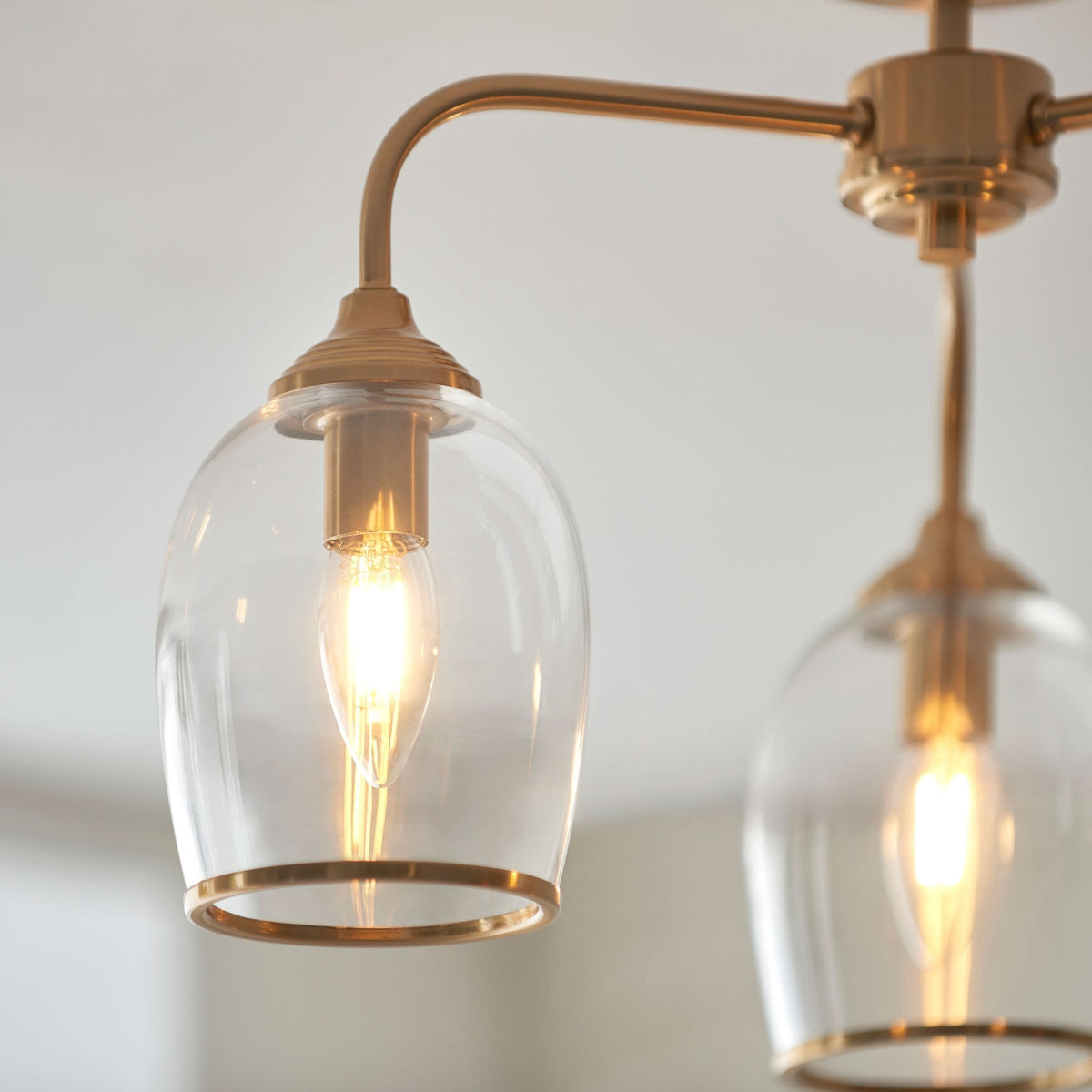 A close-up of two clear glass shades on a brass ceiling light, showing the illuminated filament bulbs.
