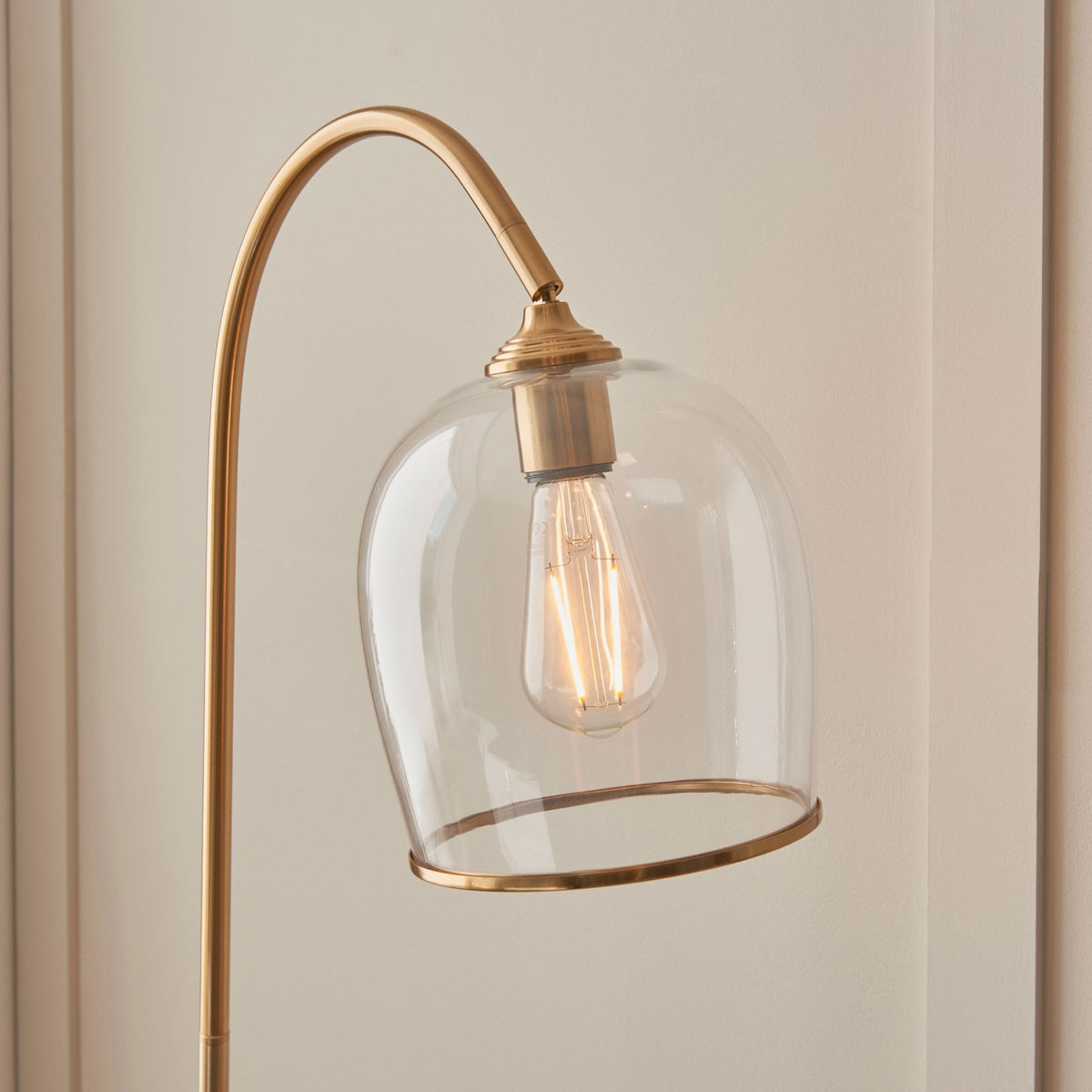 Close-up of the brass floor lamp's clear glass shade with an exposed filament bulb.