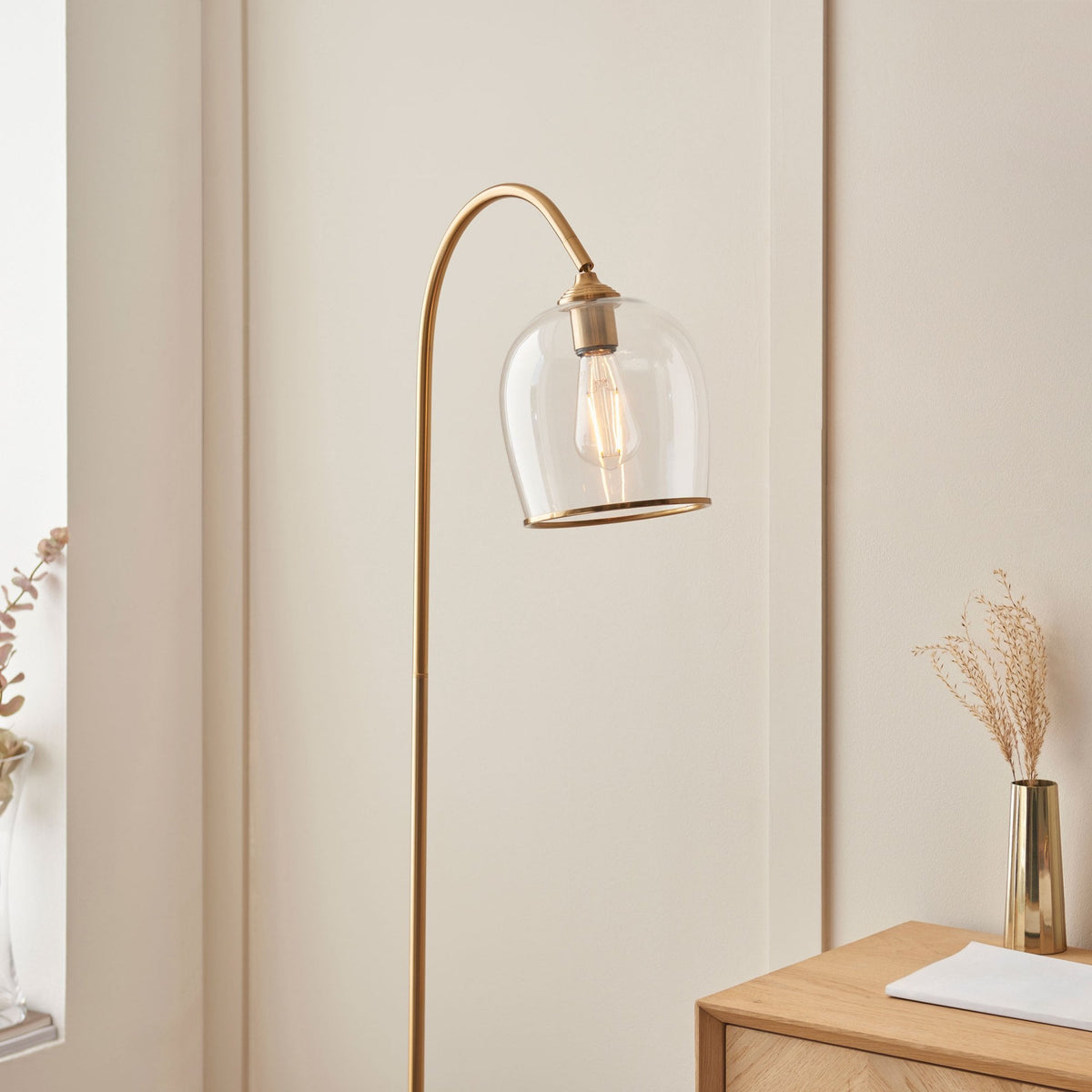 A brass floor lamp with a clear glass shade illuminates a cozy living space.