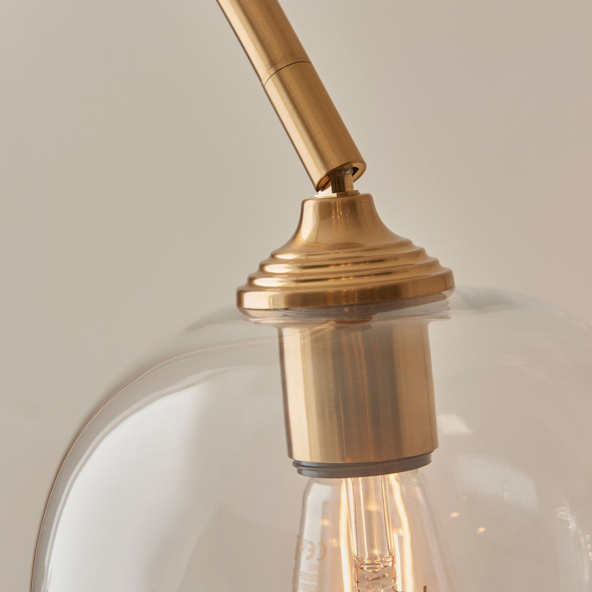 Close-up of the brass fixture holding the clear glass shade and exposed bulb of the floor lamp.