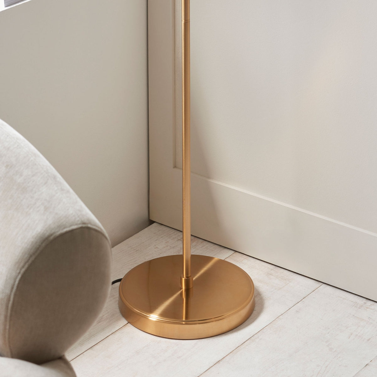 Close-up of the round brass base of the floor lamp, resting on a light wooden floor.