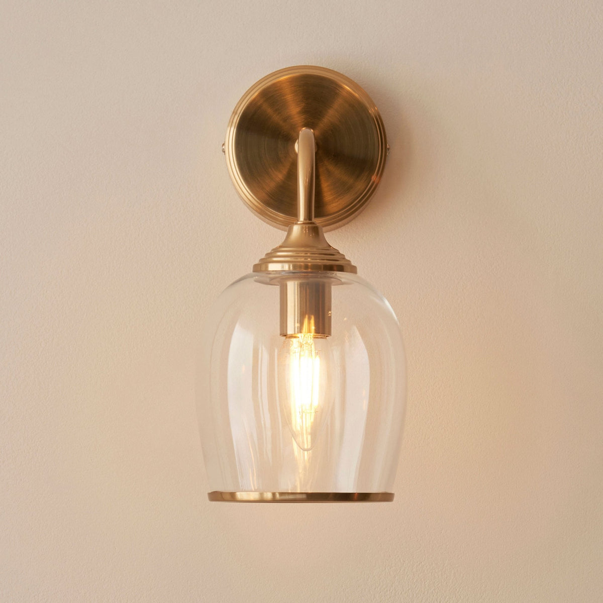 A front view of an elegant brass wall light featuring a clear glass bell shade, showcasing its intricate details.