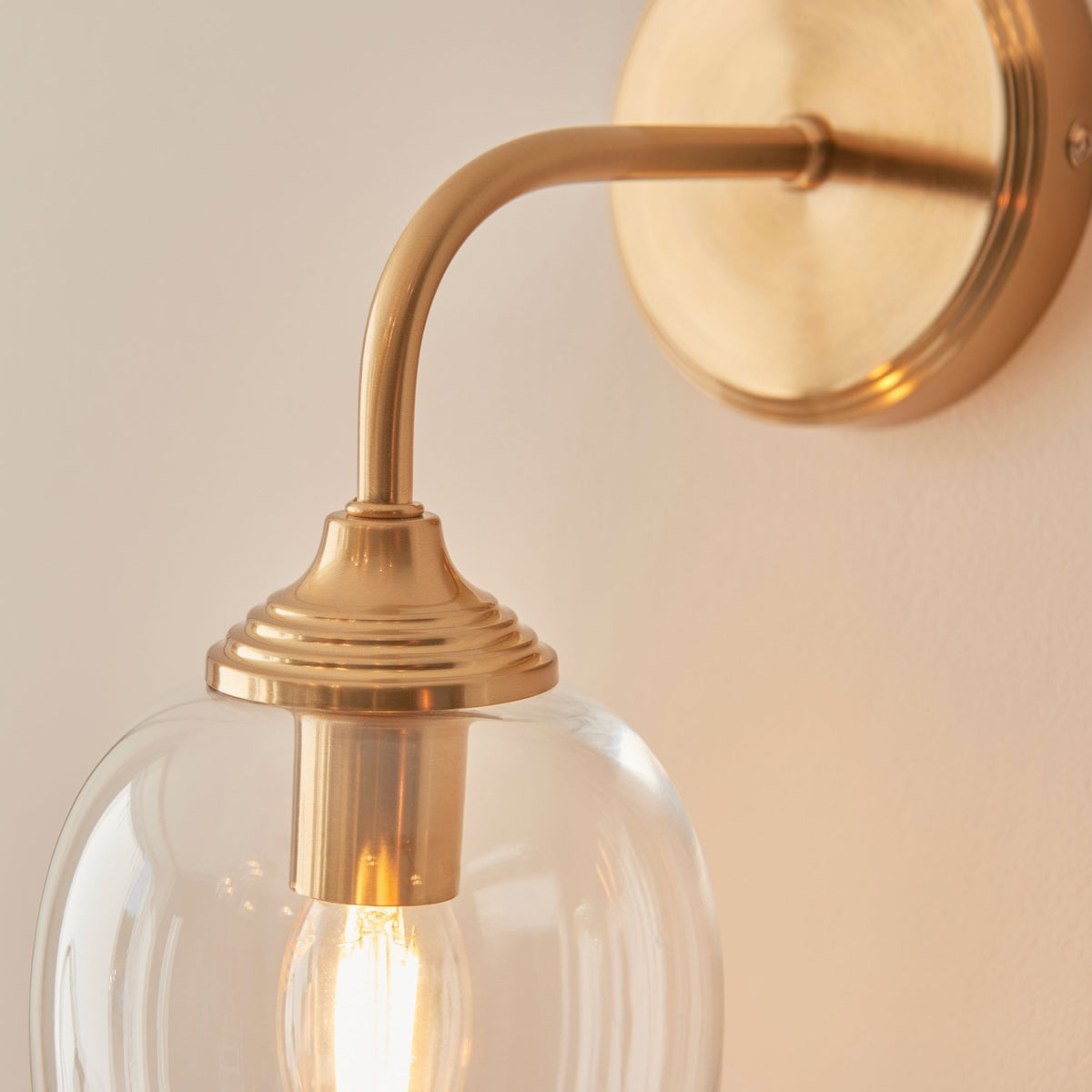 A detailed close-up of the brass fixture and clear glass shade of the wall light, highlighting its design.