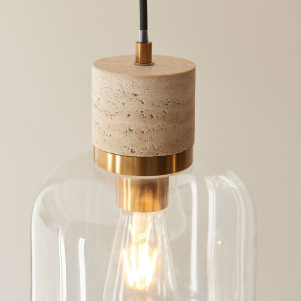 A close-up of a pendant light revealing its natural travertine stone cylinder and clear glass shade with a visible bulb.