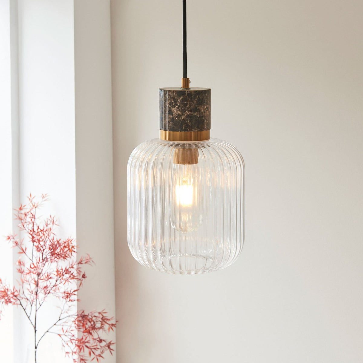 Close-up of a single modern ribbed glass pendant light with a marble and brass accent, illuminating a room.