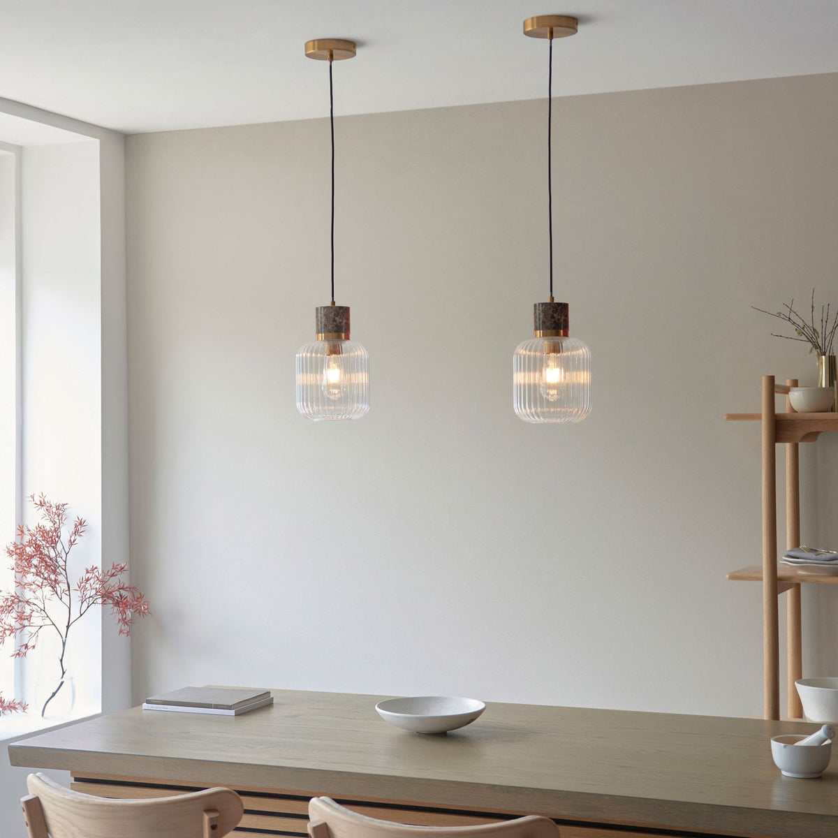 Two stylish ribbed glass pendant lights with marble accents hanging above a contemporary wooden table.