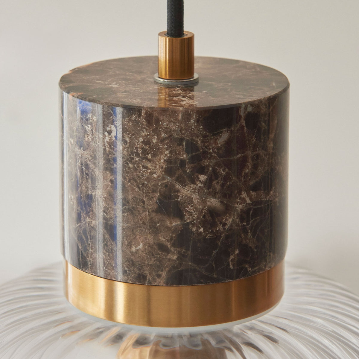 Detailed view of the rich brown marble and brass accent on top of a ribbed glass pendant light.