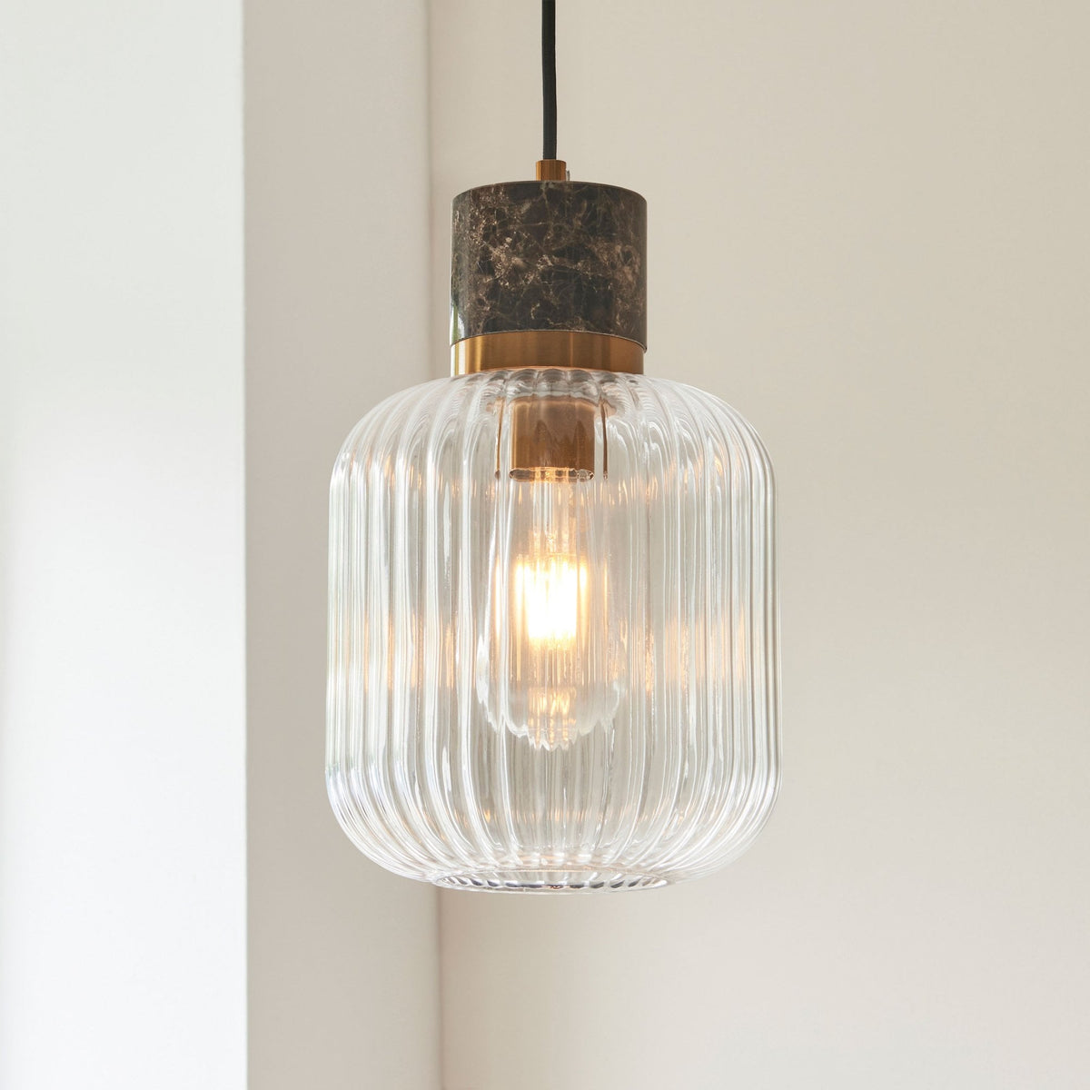 Elegant ribbed glass pendant light with a marble and brass top, showcasing its warm glow against a soft background.