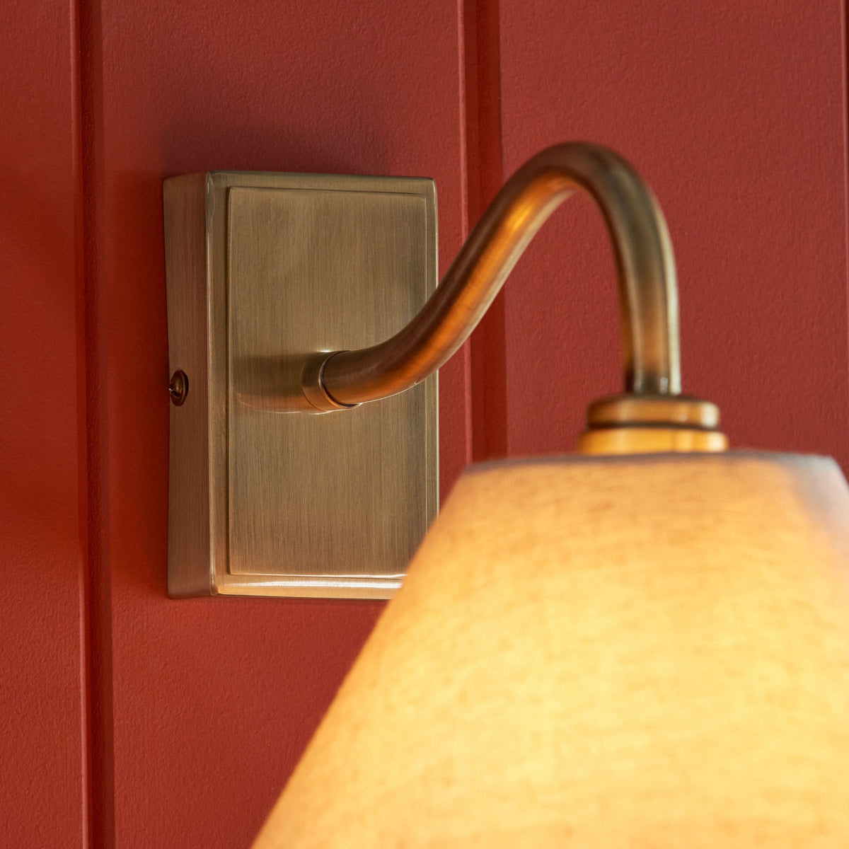 Primer plano de un aplique de pared de latón antiguo con luz cálida en una pared de madera roja.
