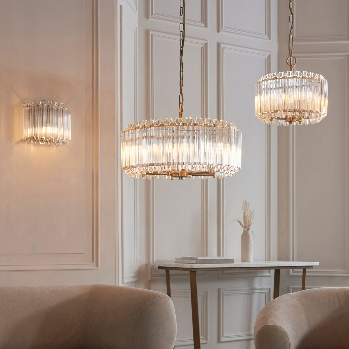 Multiple golden chandeliers and a wall sconce with glass rods illuminate a beautifully decorated room.
