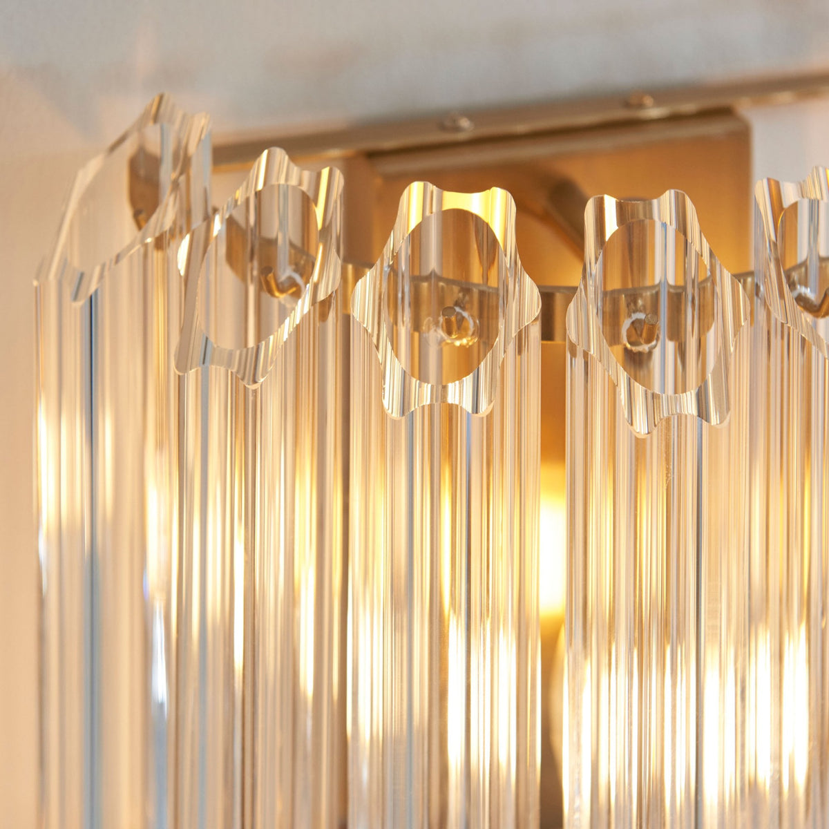A close-up of a crystal wall light, highlighting the faceted crystal rods and the warm glow of the bulb within.
