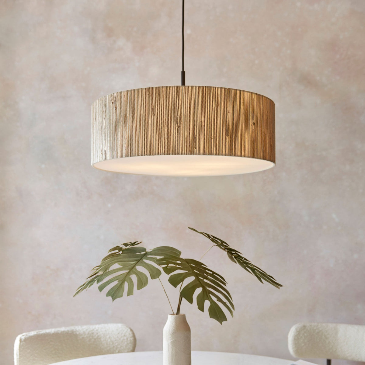 A close-up of a pendant light with a wide, drum-shaped shade made from natural light wood slats.