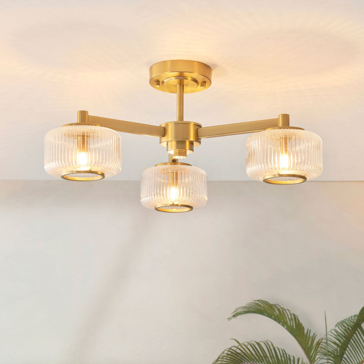 Un plafonnier doré à trois bras avec des abat-jour en verre cannelé illuminant le plafond.