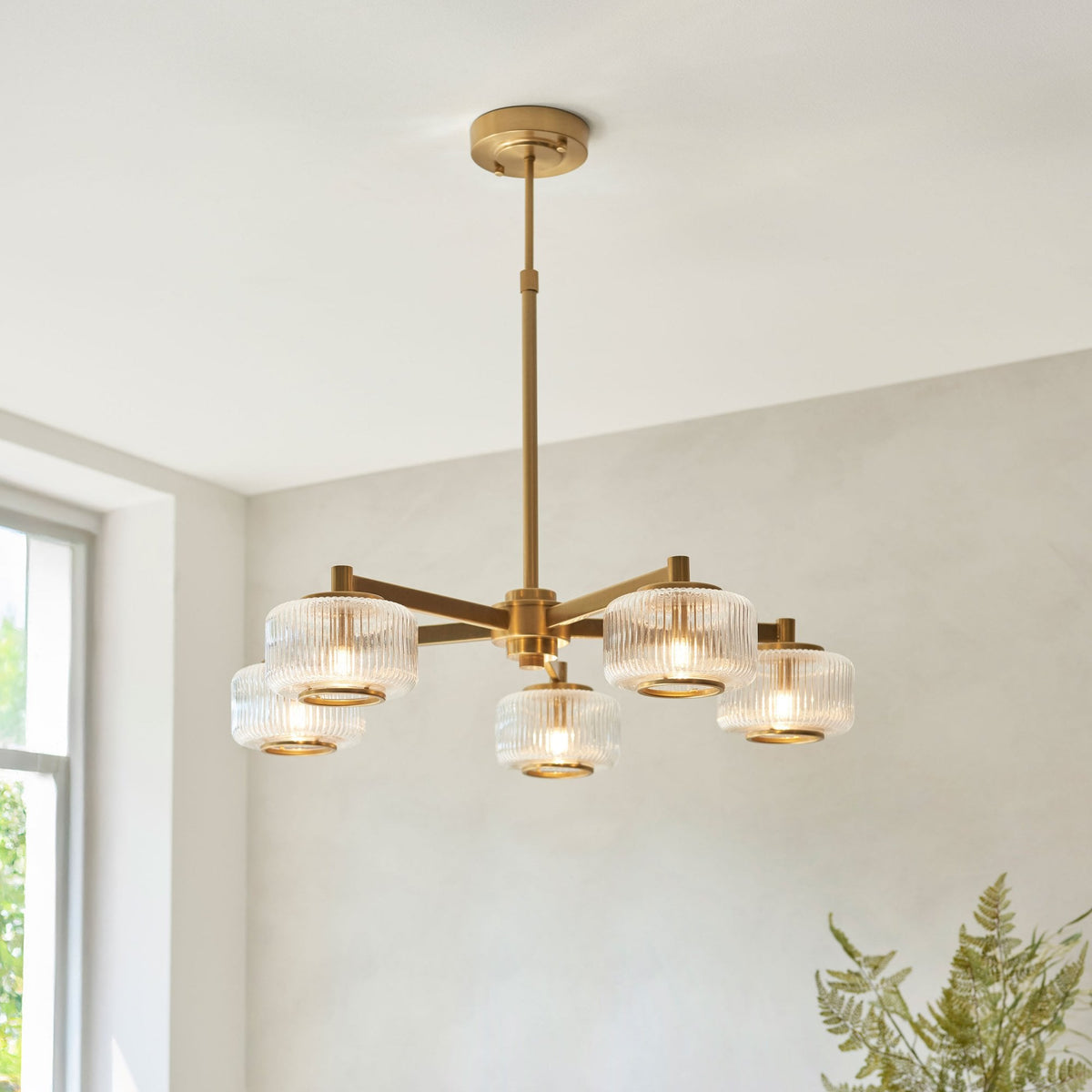 Un candelabro dorado moderno con cinco bombillas de cristal acanalado en un comedor luminoso.