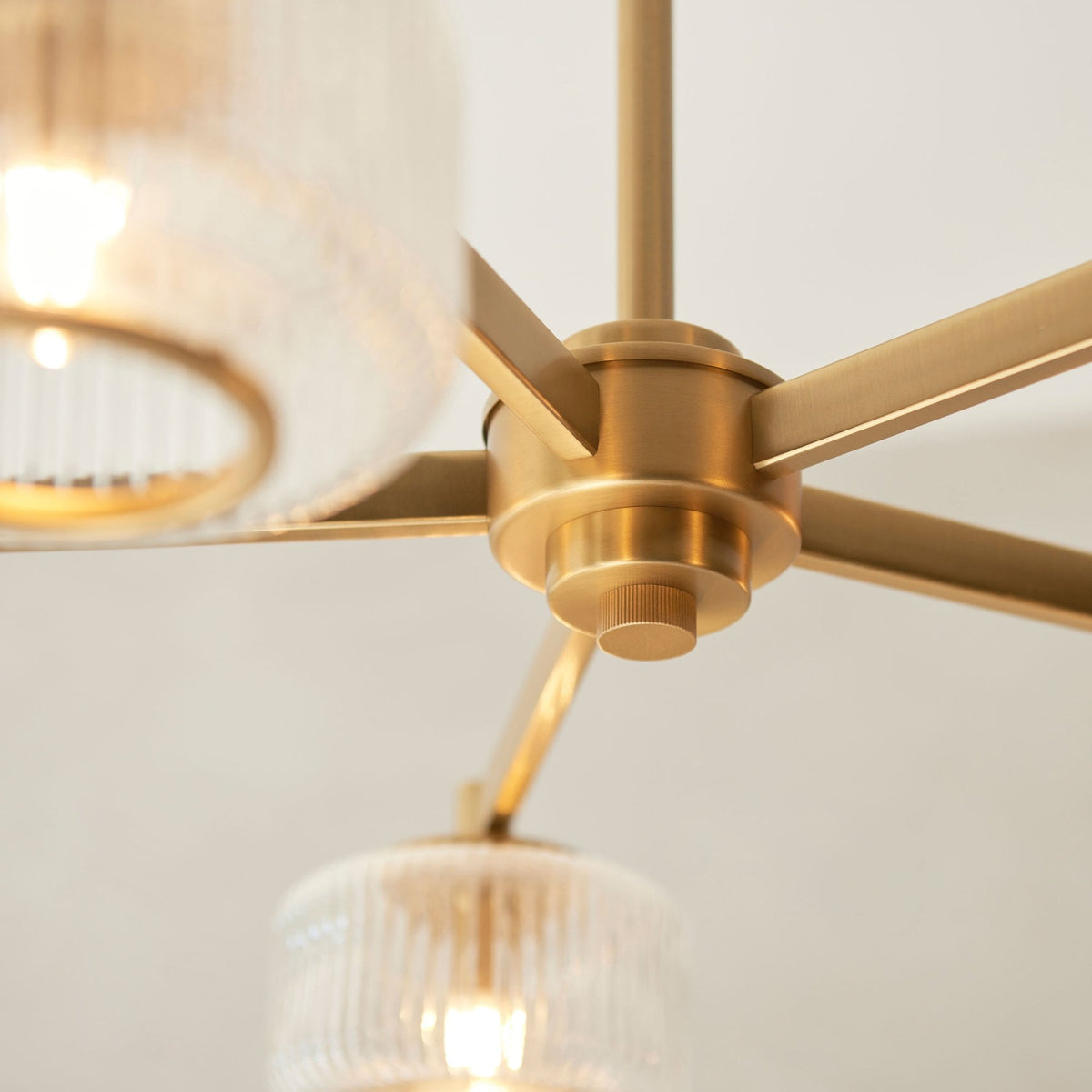 Primer plano de una luz de candelabro dorada con pantalla de cristal acanalado y bombillas brillantes.