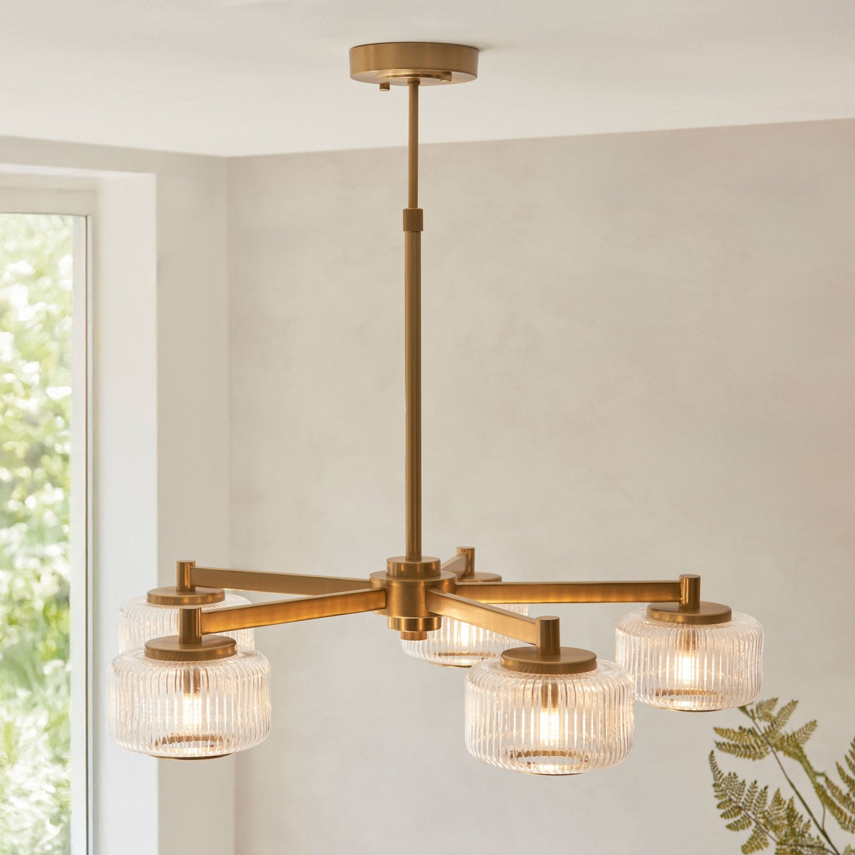 Un candelabro moderno con cuatro luces y pantallas de cristal estriado sobre un fondo de ventana.