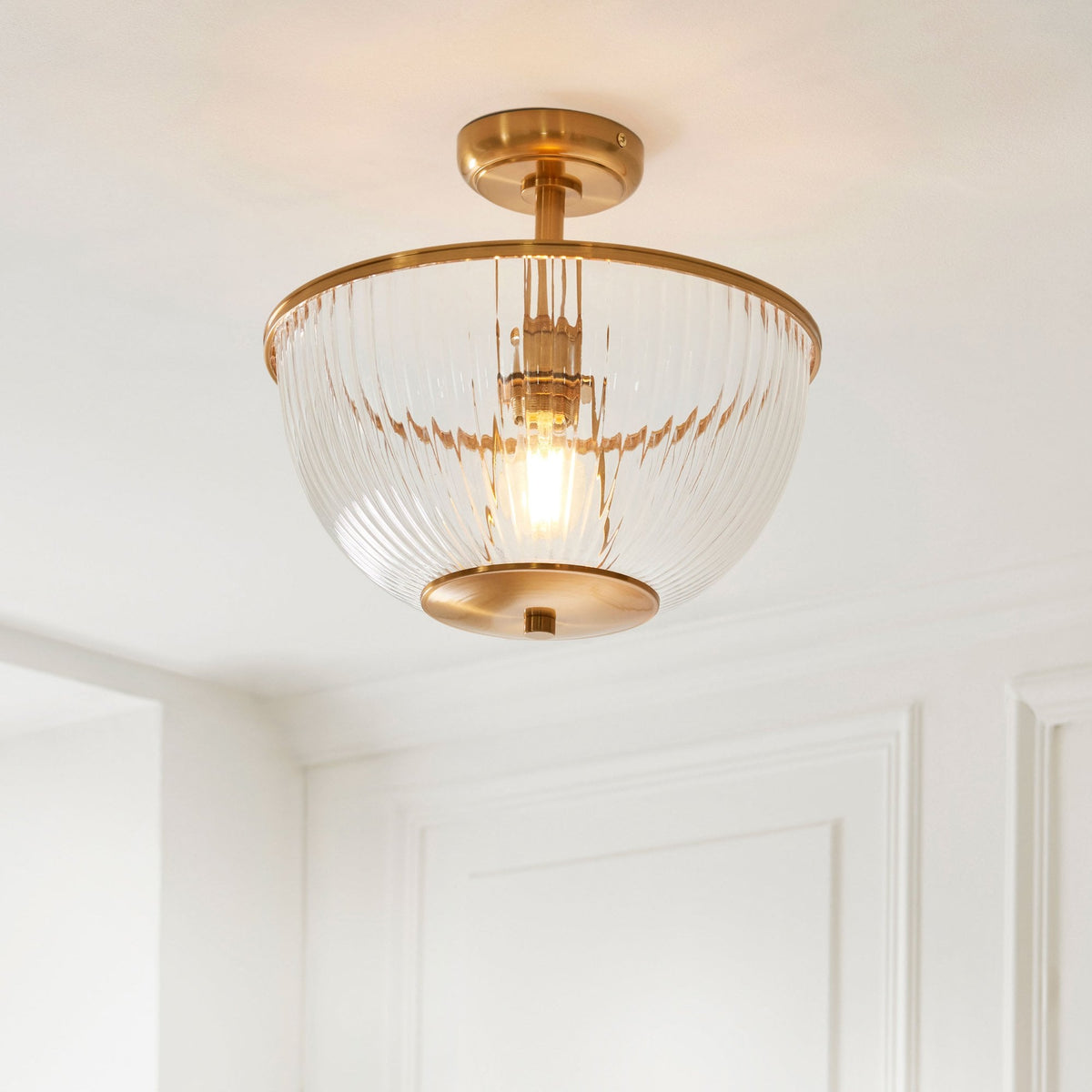 A close-up view of the ribbed glass and brass semi-flush mount ceiling light on a white ceiling.