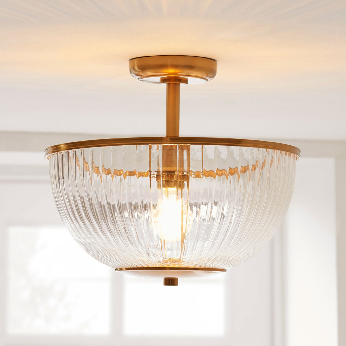 A semi-flush mount ceiling light with a ribbed glass shade and brass accents illuminates a room.