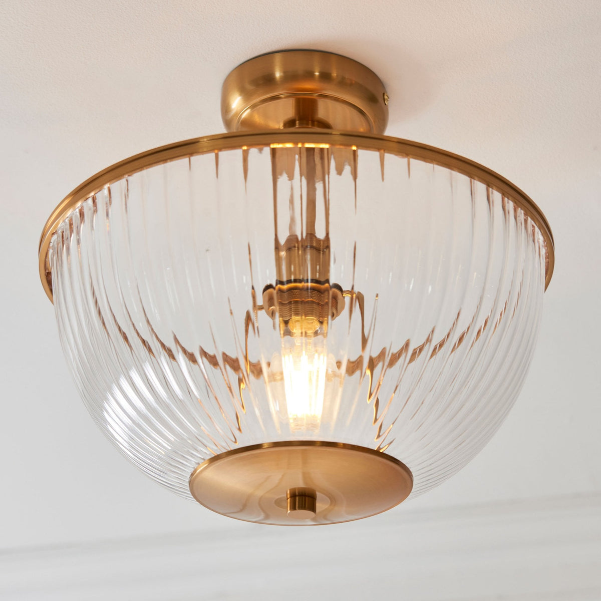 A close-up of a semi-flush mount ceiling light with a ribbed glass dome and brass fittings.