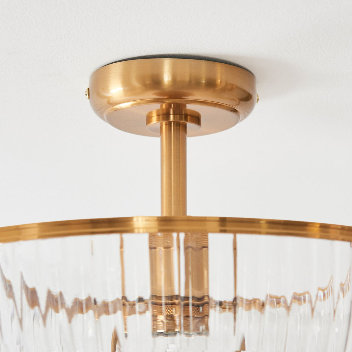 A close-up of the antique brass ceiling rose and stem supporting the ribbed glass shade.