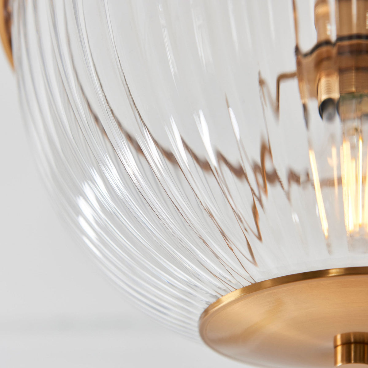 A detailed close-up of the ribbed clear glass shade and the brass base of the ceiling light.