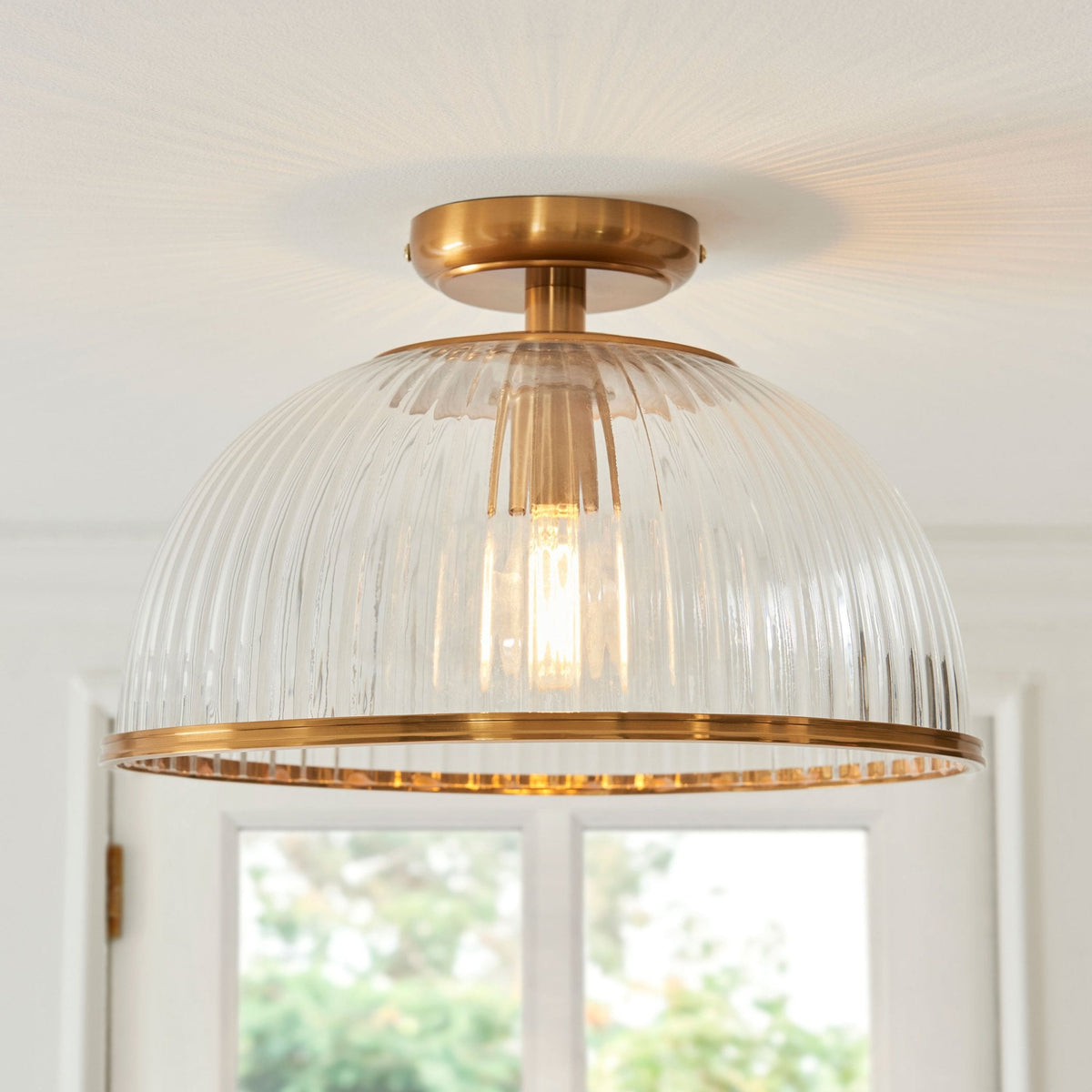 A close-up of a clear, ribbed glass ceiling light with a brass base and trim, shining brightly.
