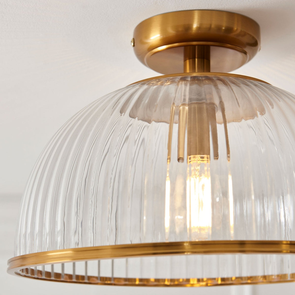 A close-up of the ribbed glass shade and brass trim of the ceiling light, showcasing its texture.