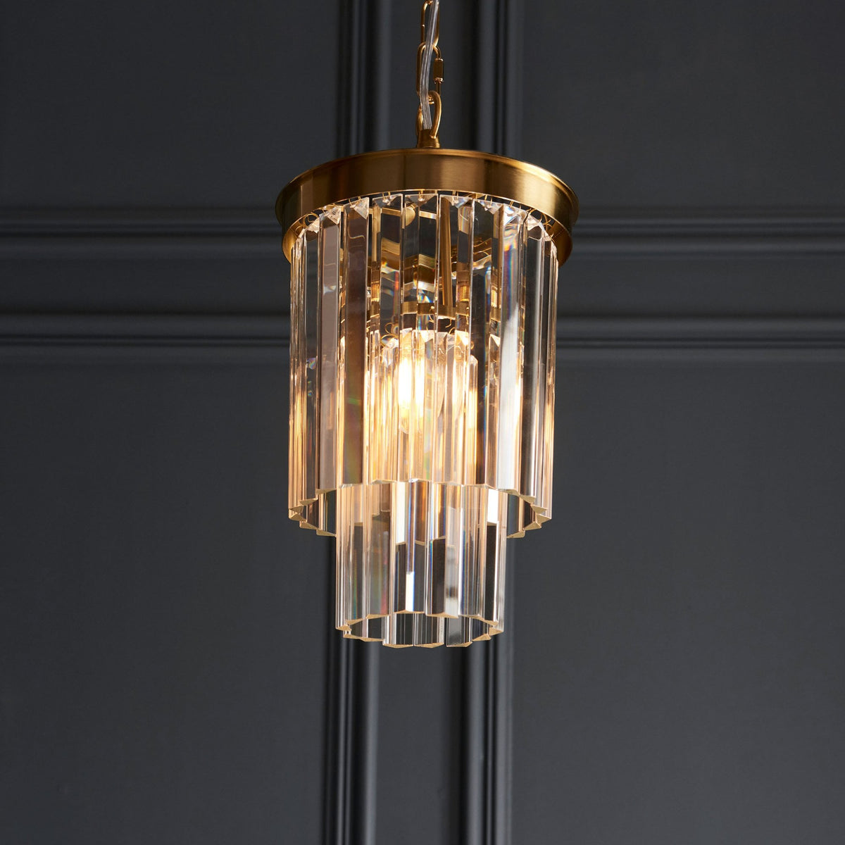 A close-up shot showing an illuminated pendant light, which features a brass frame and tiered clear glass rods.