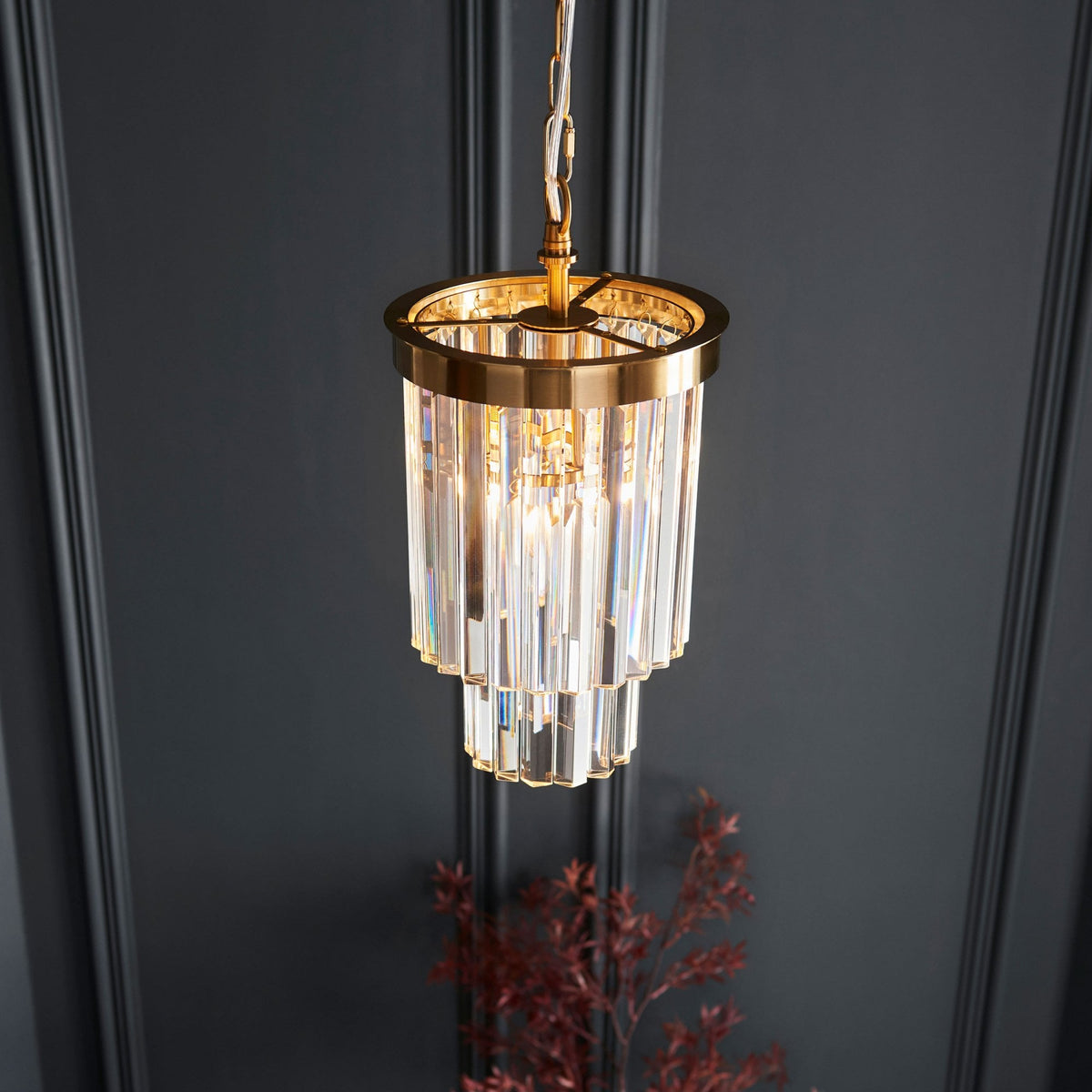 An elevated shot showing an illuminated pendant light, which features a brass frame and tiered clear glass rods.