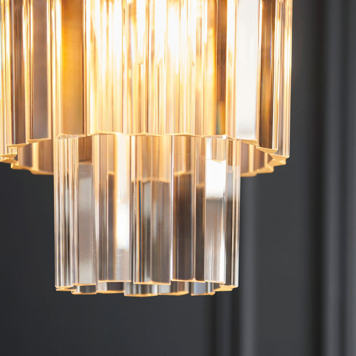 A close-up shot of the pendant light, focusing on the illuminated clear glass rods and the golden glow they emit.