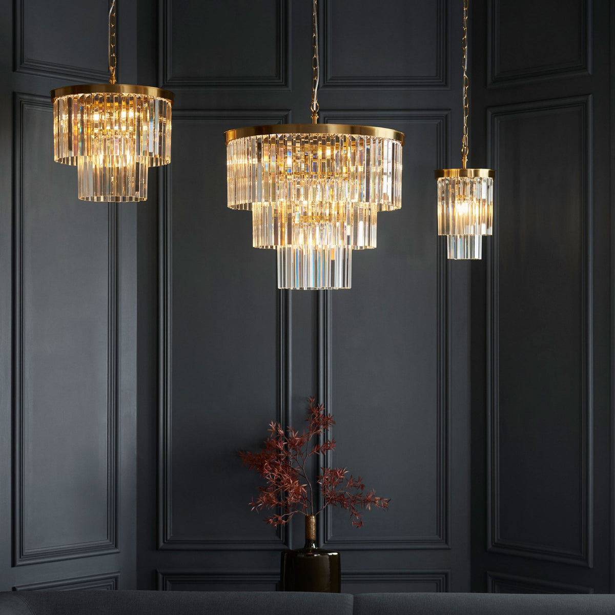 Three pendant lights of different sizes, featuring brass frames and clear glass rods, illuminated in a dark room.