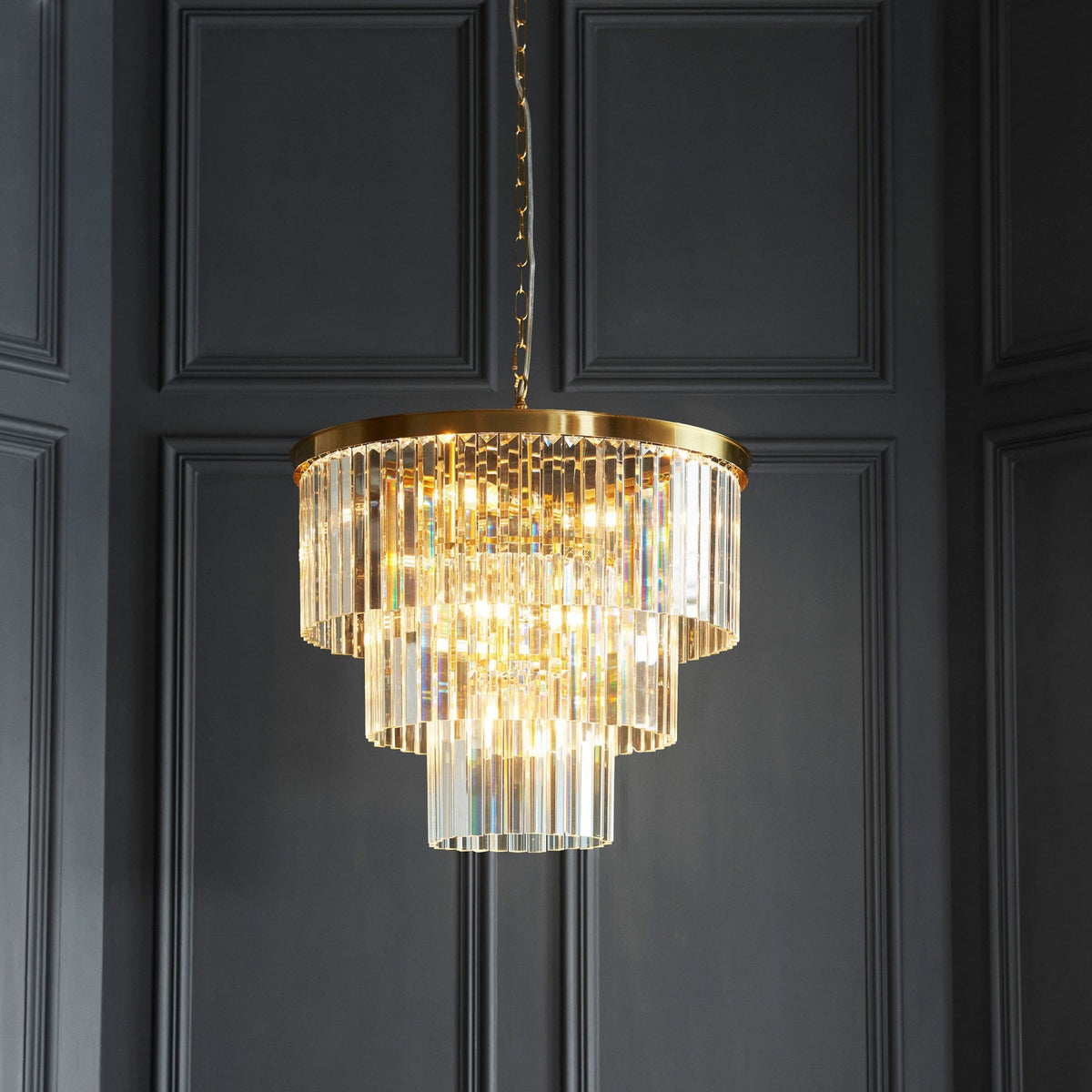 A sparkling chandelier with three tiers of clear crystal rods hangs in a room with dark paneled walls.