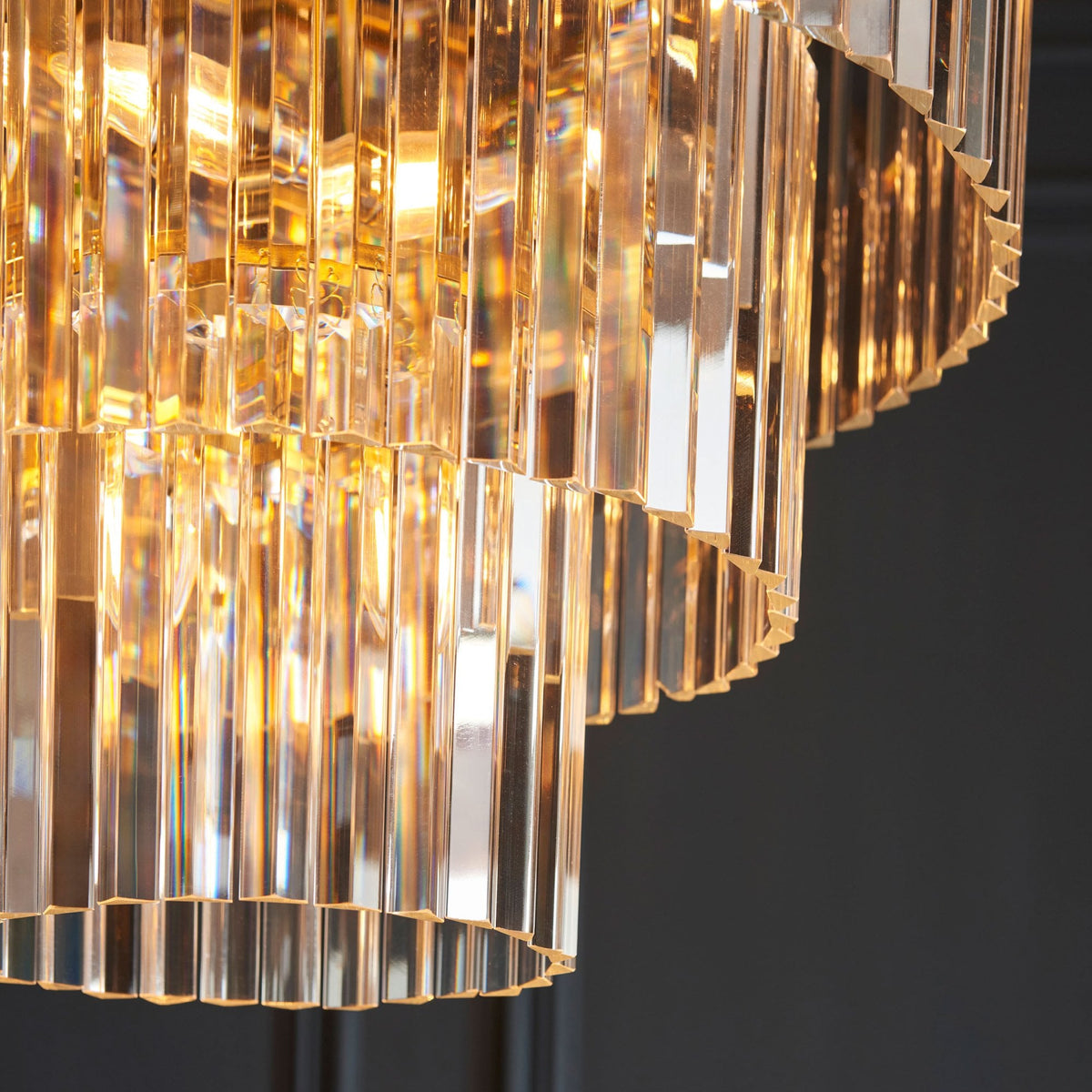 A close-up view of the tiered crystal rods of a chandelier, reflecting warm light against a dark background.