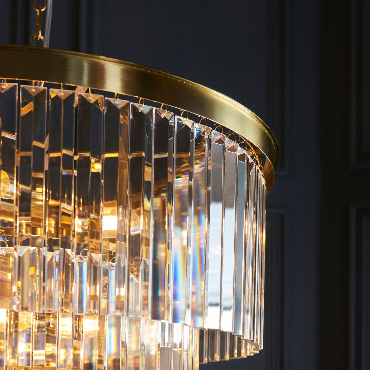A detailed close-up of the elegant brass rim and sparkling crystal rods of a luxurious chandelier.